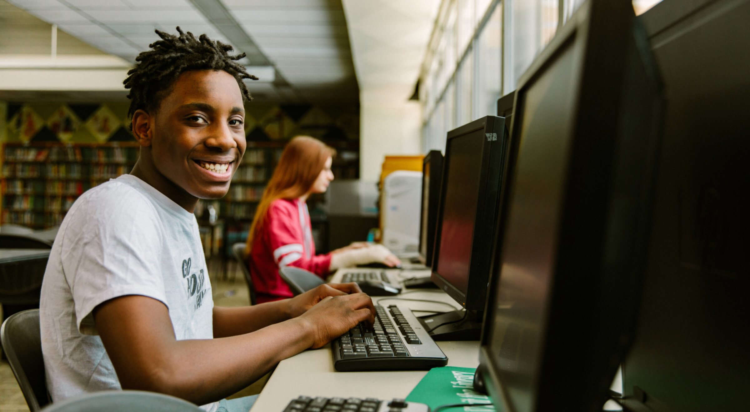 Garçon souriant devant un ordinateur dans une bibliothèque