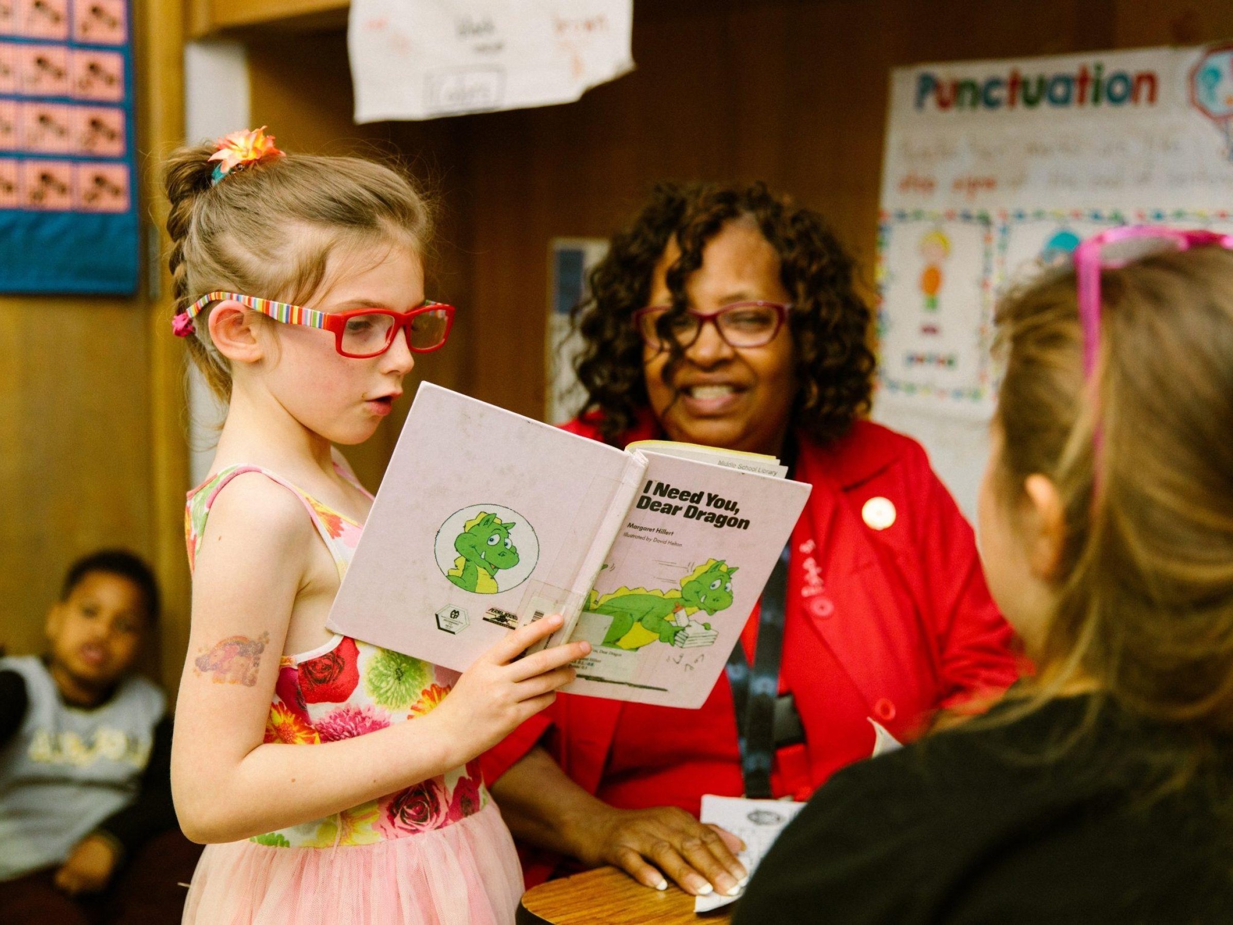 Una alumna de primaria lee un libro a un adulto que visita su clase