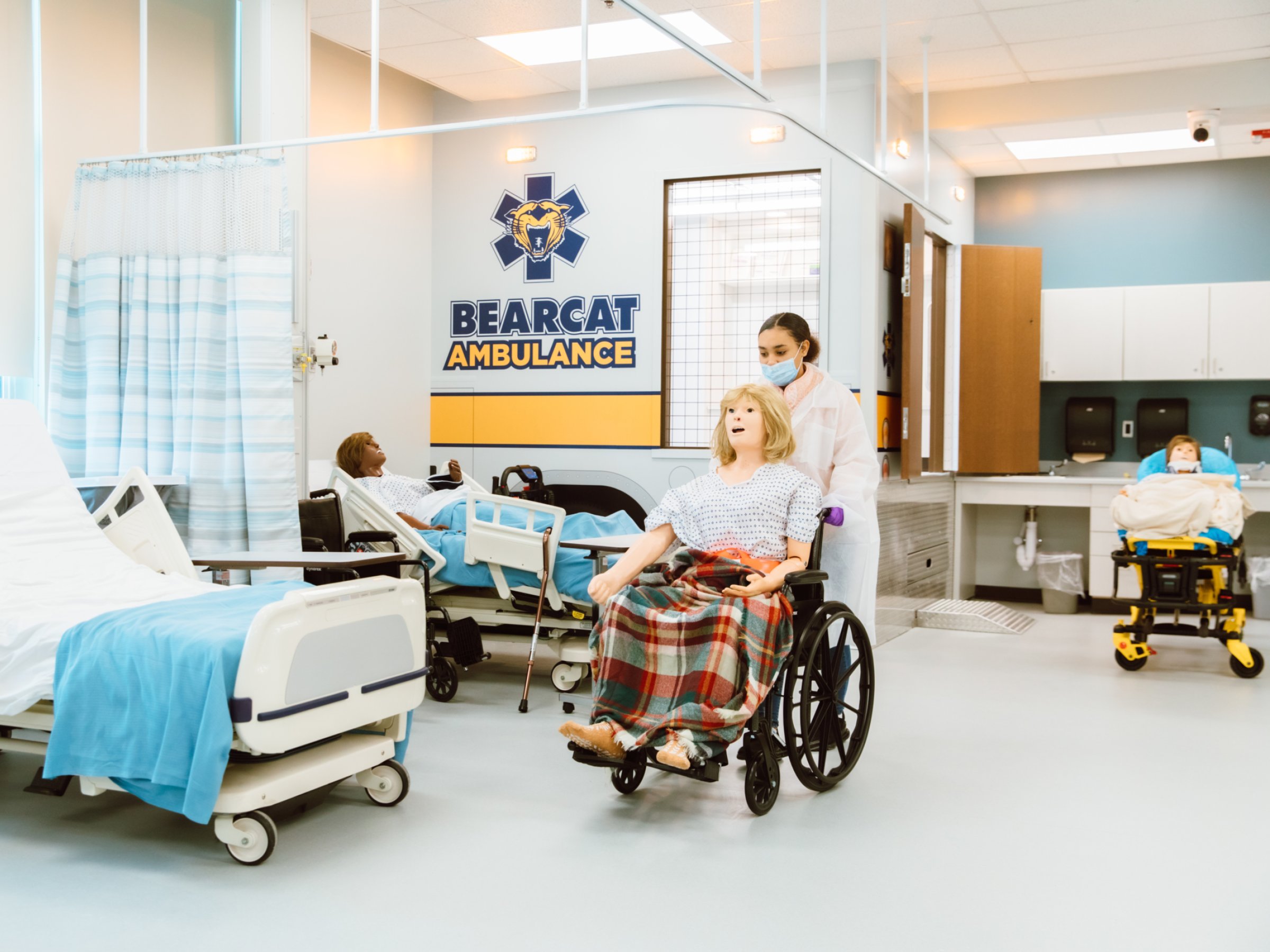 Un estudiante de las Academias Profesionales BCCHS empuja un maniquí en una silla de ruedas dentro del nuevo Laboratorio de Simulación de Atención Sanitaria.