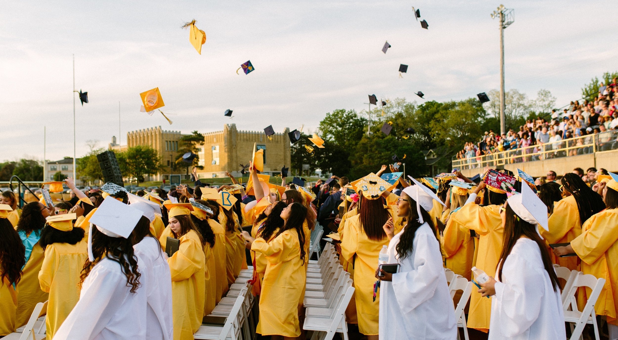 Cérémonie de remise des diplômes avec des étudiants portant des casquettes et des toges jaunes et blanches et jetant leurs casquettes en l'air en signe de célébration.